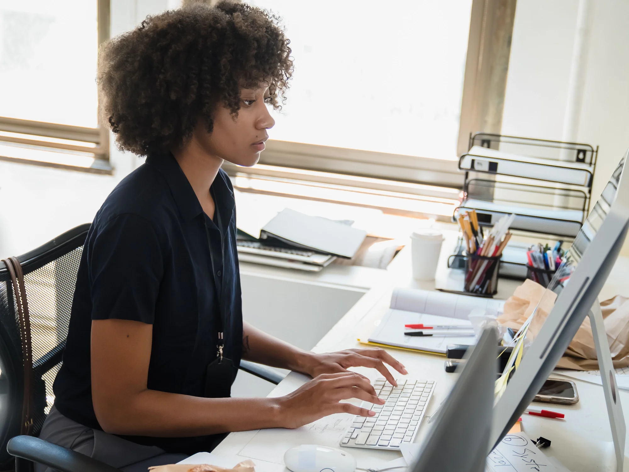A woman working at a desktop computer beside a sunlit window